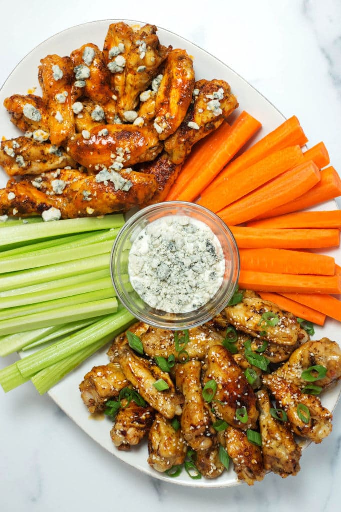 Overhead view of white platter with chicken wings, carrots, celery, and blue cheese dressing