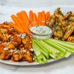 A white platter with a blow of blue cheese dressing, carrots, and celery in the center, chicken wings on the edges
