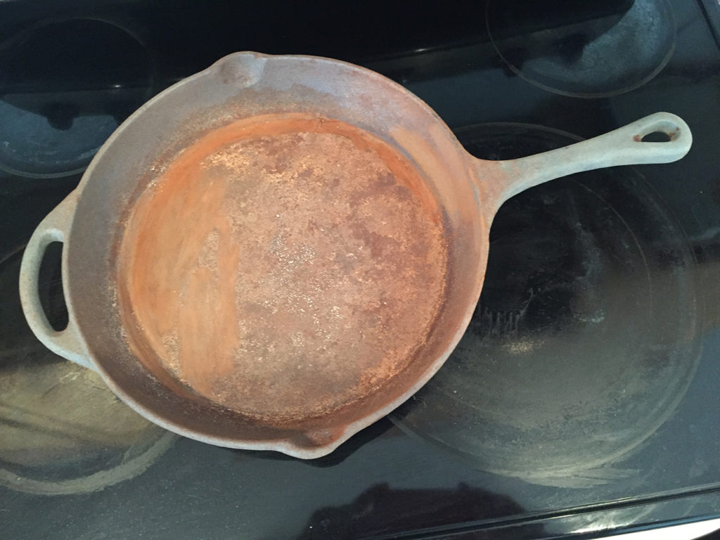 Overhead view of a rusty cast iron skillet on a black cooktop