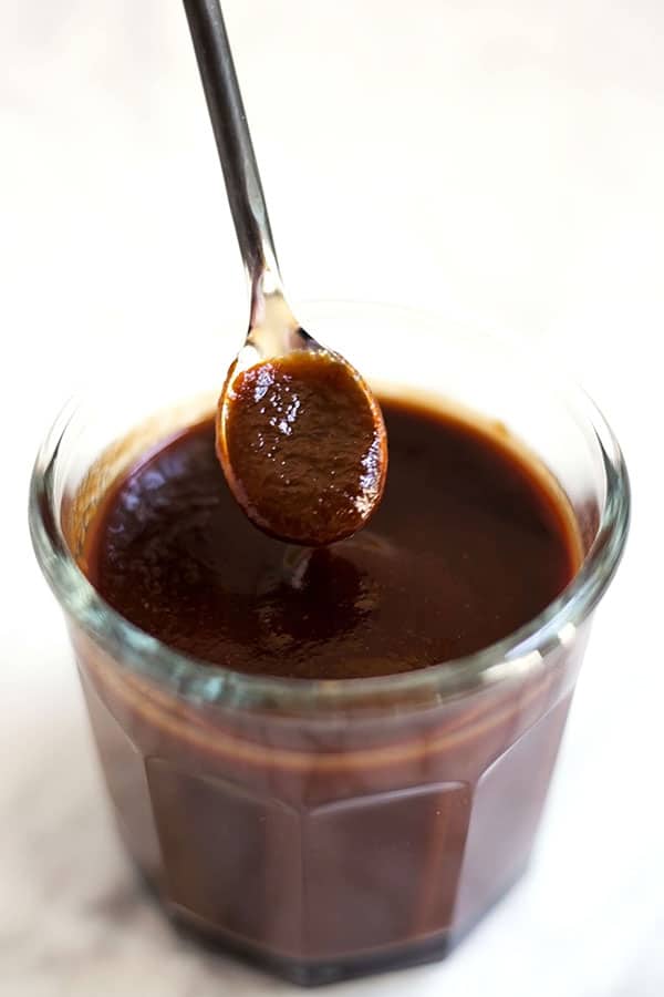 A clear jar of bbq sauce with a spoon