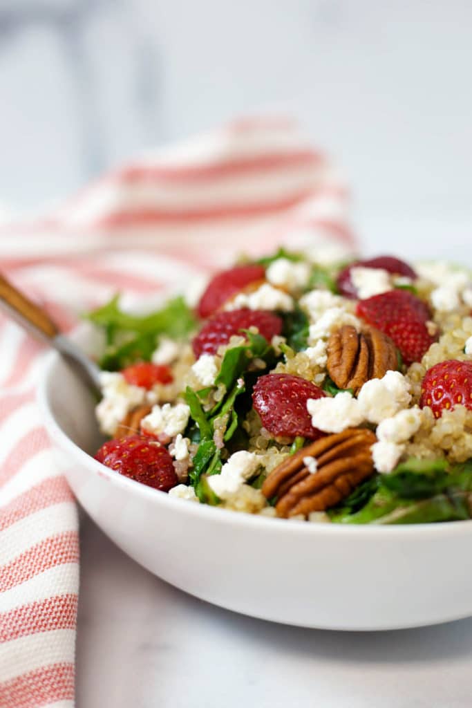 Side view of a white bowl of salad with strawberries, goat cheese, and pecans