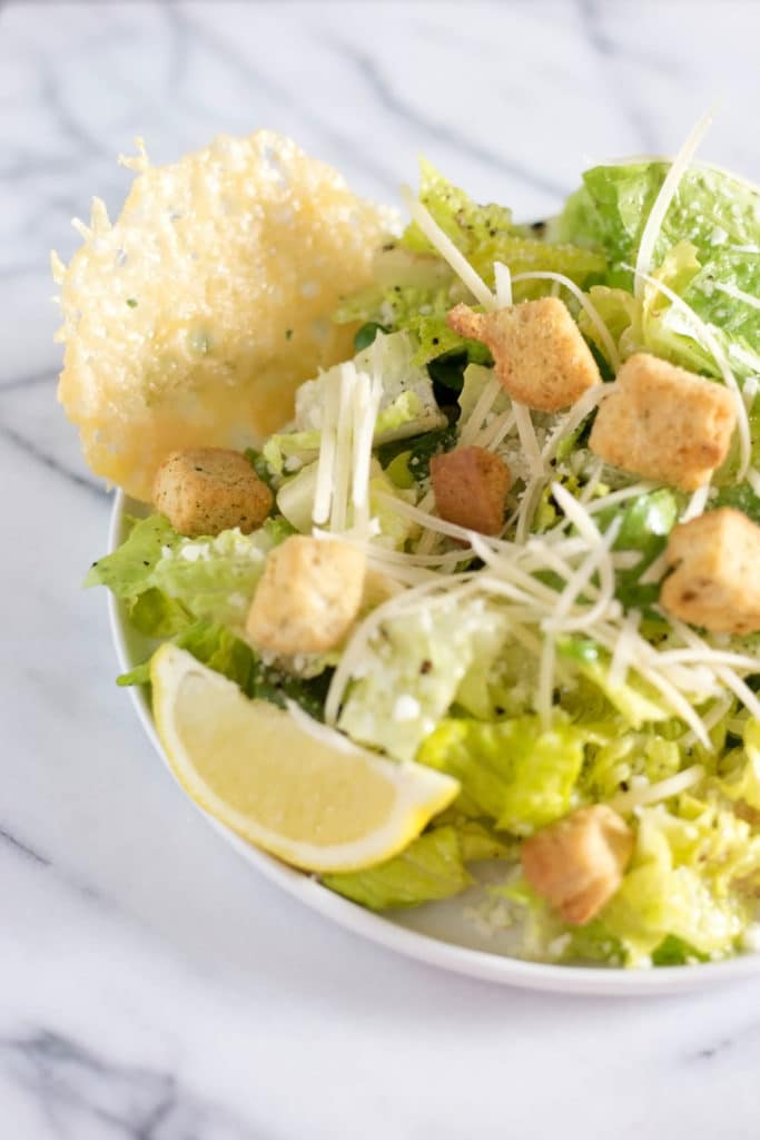 bowl of caesar salad with croutons, grated parmesan cheese, a slice of lemon, and a cheese crisp