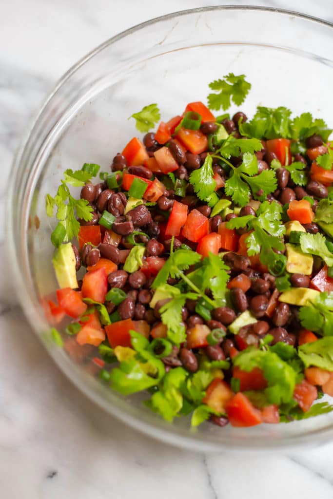Clear bowl of salad with chopped tomatoes, avocado, cilantro, and black beans