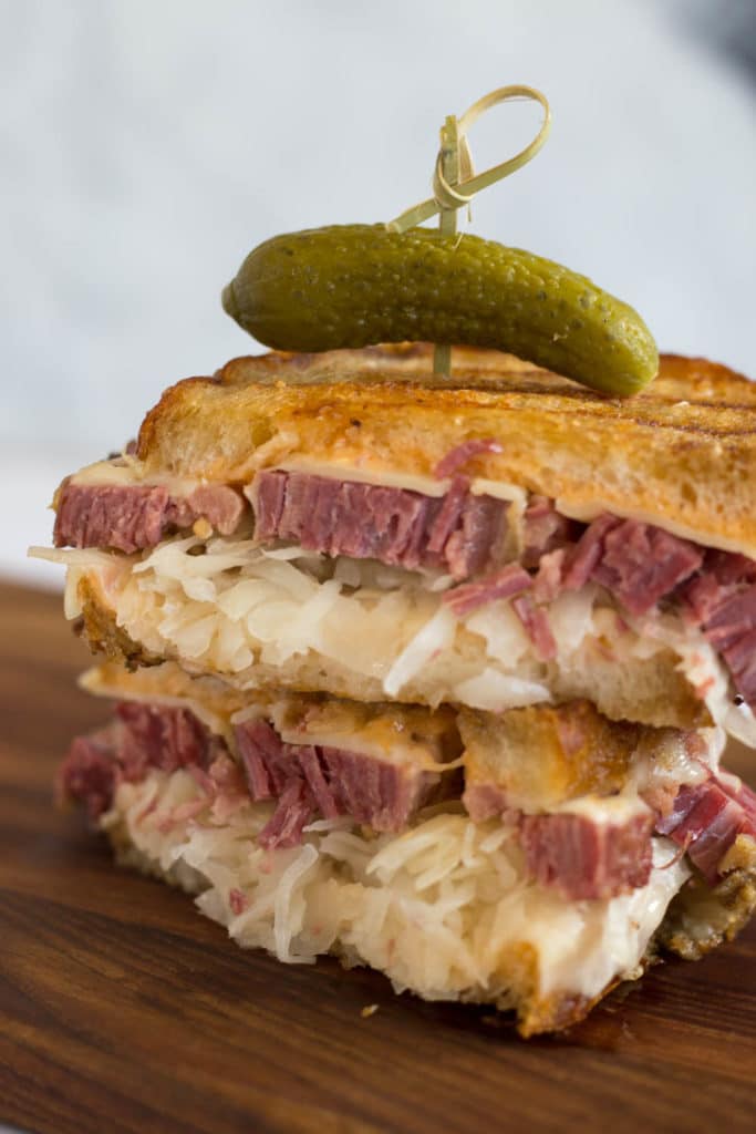 Two halves of reuben sandwich stacked and toothpick with pickle on top