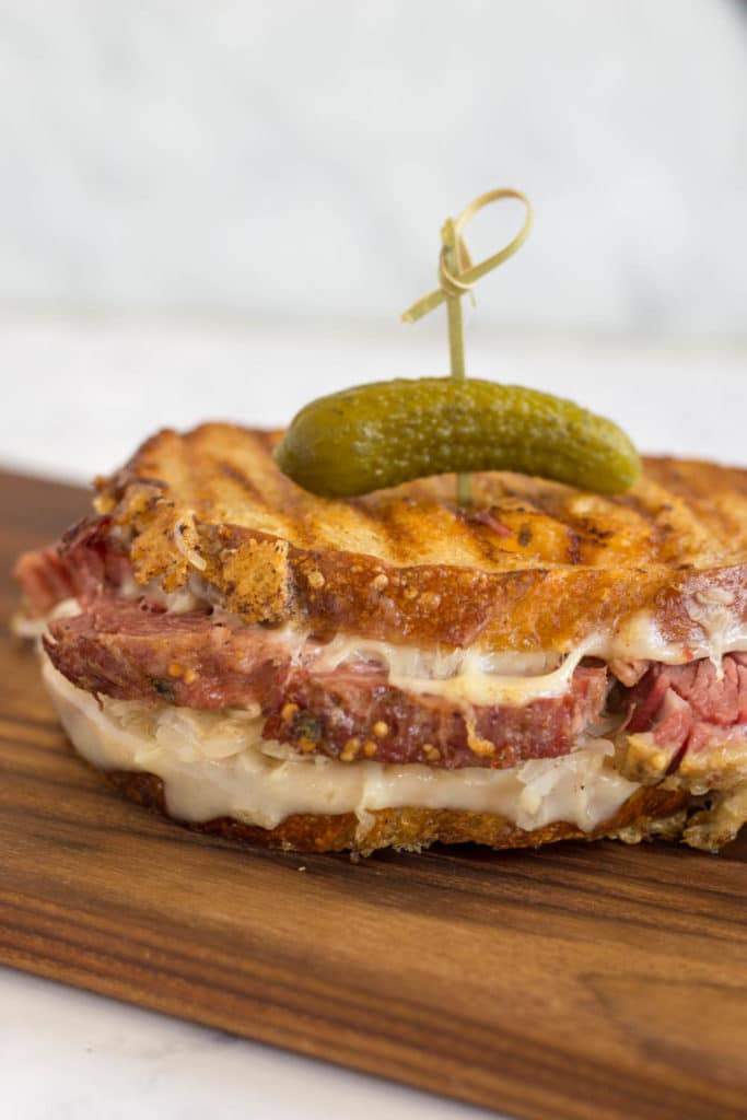 Toasted reuben sandwich on a cutting board and toothpick with pickle in the top