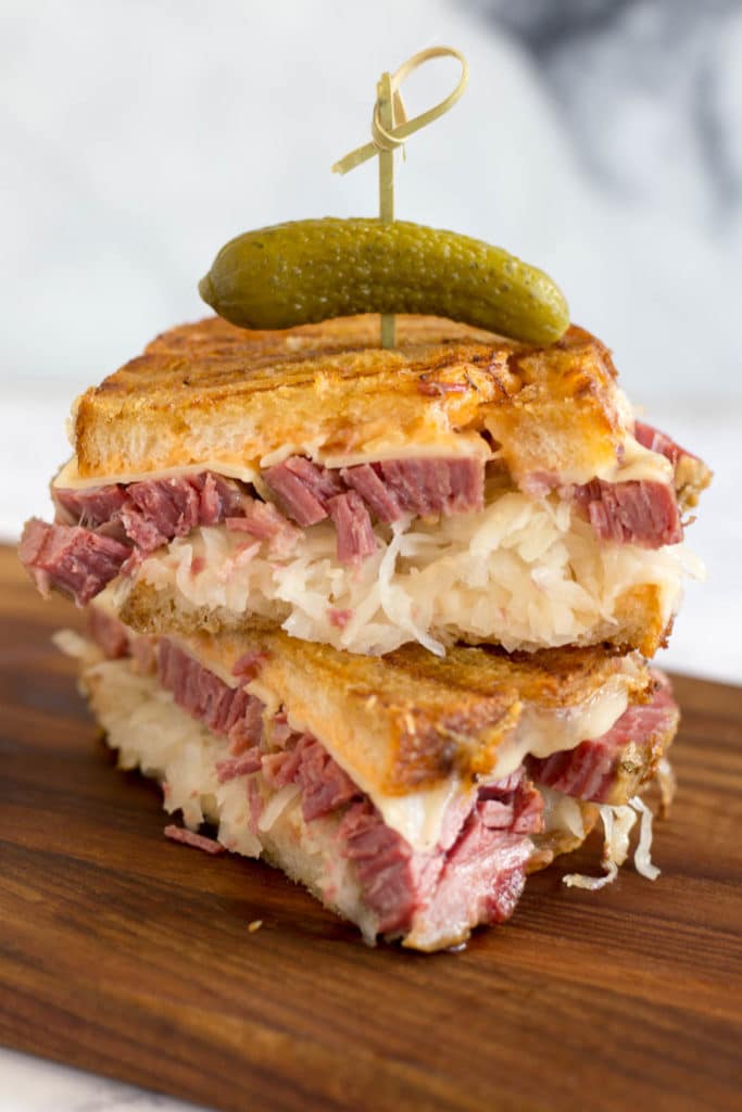 Two halves of a reuben sandwich stacked and a toothpick with pickle in the top