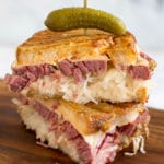 Two halves of a reuben sandwich stacked and a toothpick with a pickle in the top