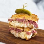 Two halves of reuben sandwich stacked and toothpick with pickle on top