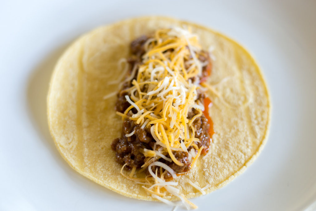 Corn tortilla topped with ground beef and shredded cheddar cheese