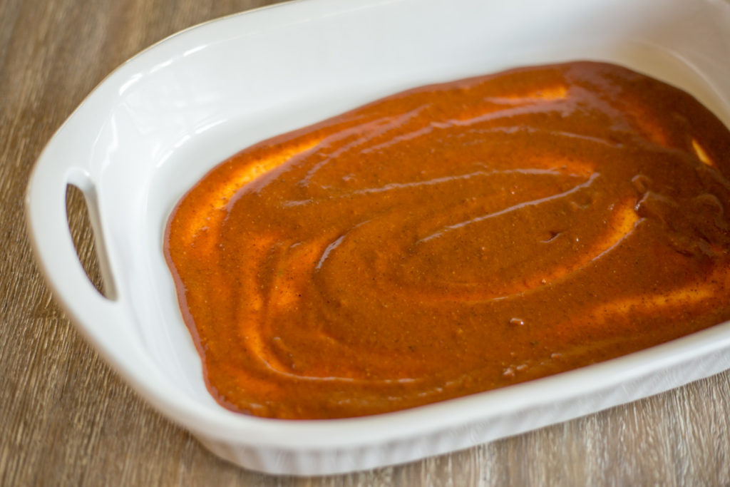 White baking dish with red sauce spread on bottom