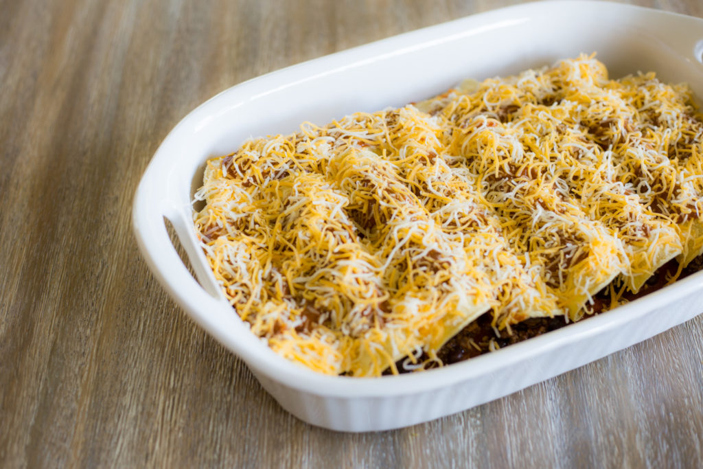 White baking dish filled with uncooked beef enchiladas topped with cheddar cheese