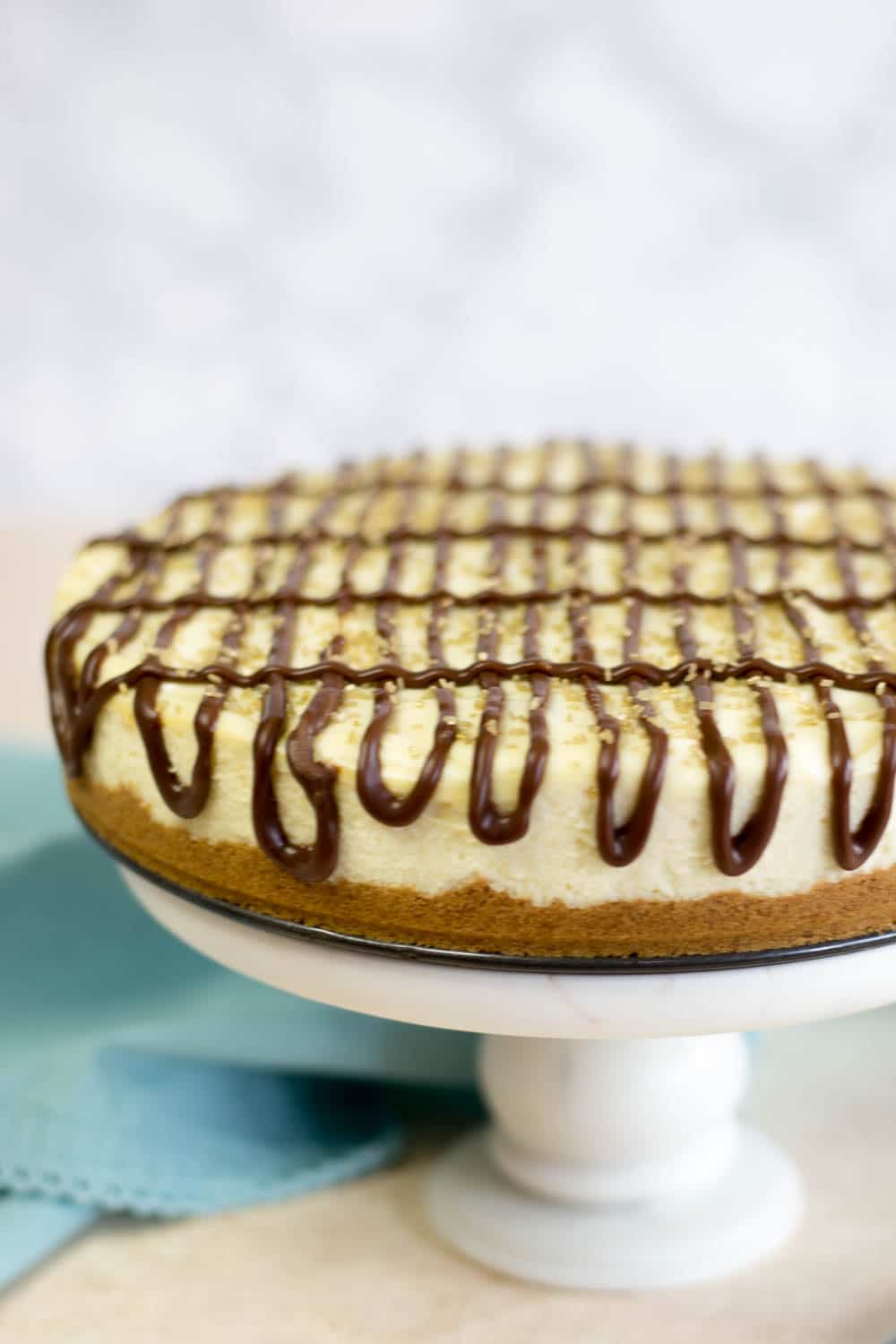 A white cake stand topped with a cheesecake that is drizzled with chocolate