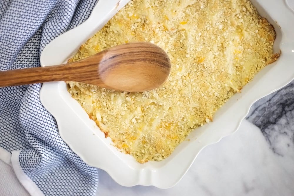 Overhead view of white baking dish filled with hash brown casserole with a spoon on top