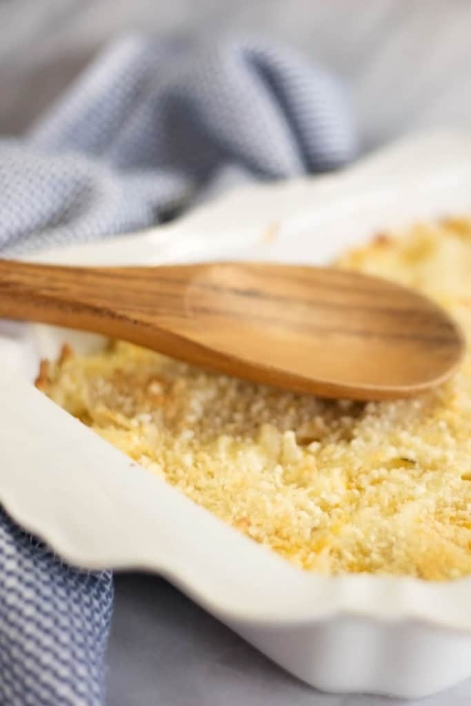 White baking dish filled with hash brown casserole and a wooden spoon on top