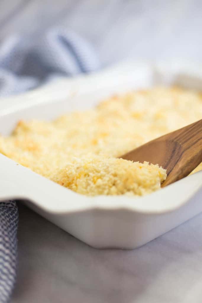 A wooden spoon scooping from a white baking dish of hash brown casserole