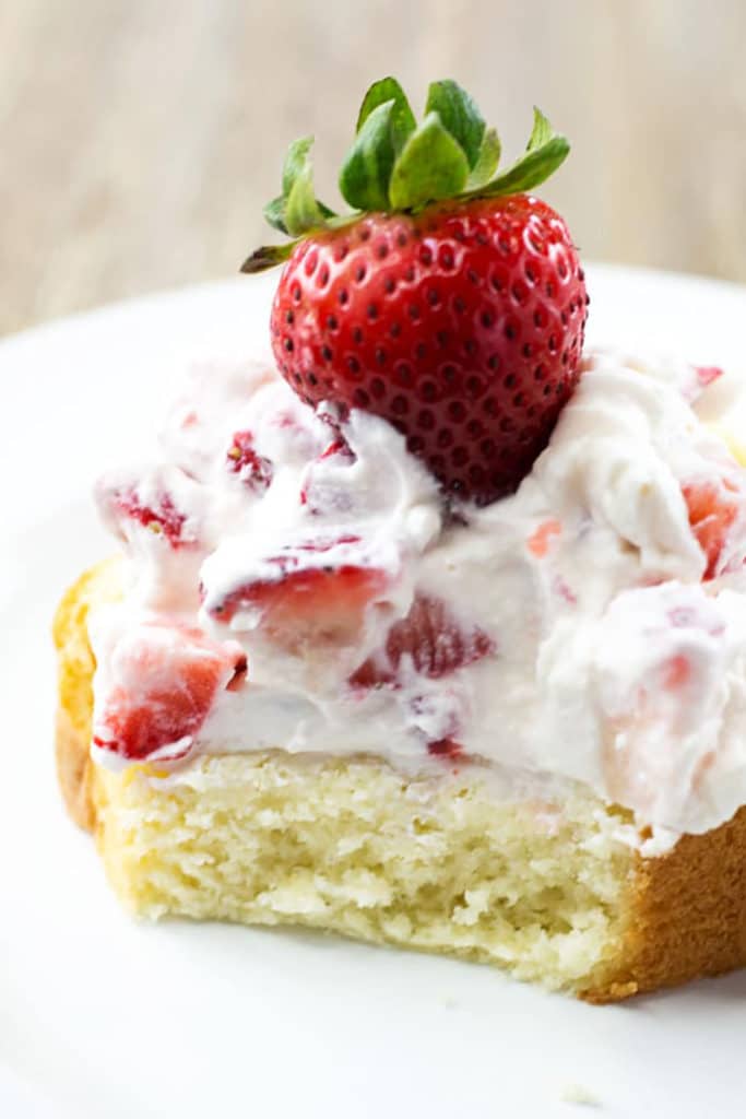 A piece of pound cake with a bite out of it topped with strawberries and whipped cream