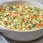 A tan skillet with a baked sausage, tomato, spinach, and cheese frittata