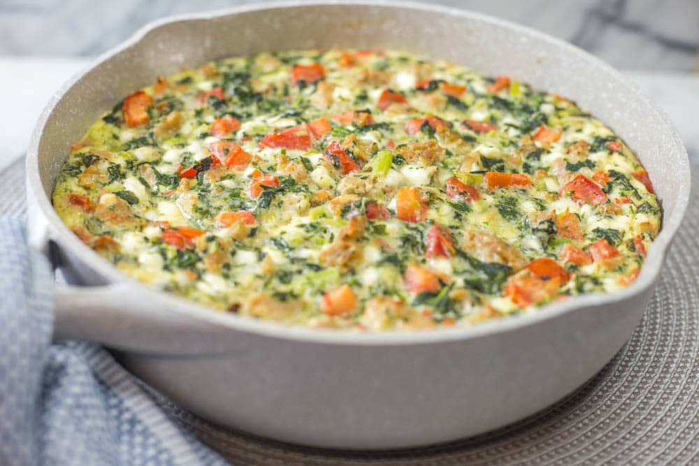 A tan skillet with a baked sausage, tomato, spinach, and cheese frittata