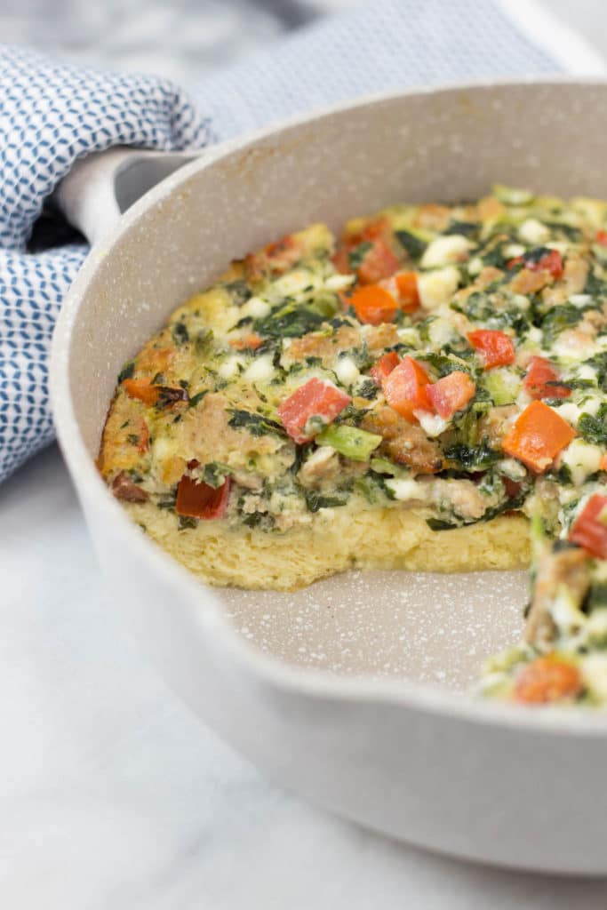 Tan skillet with a slice removed from a sausage, tomato, spinach and cheese frittata