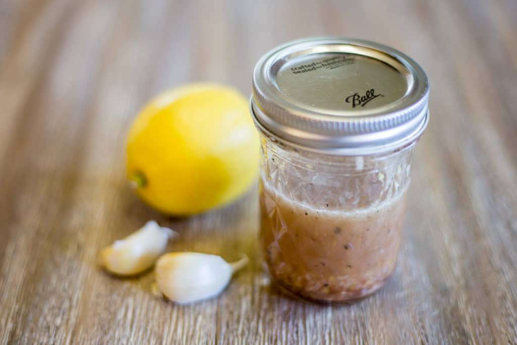 A mason jar filled with a vinaigrette, 2 cloves of garlic, and a lemon