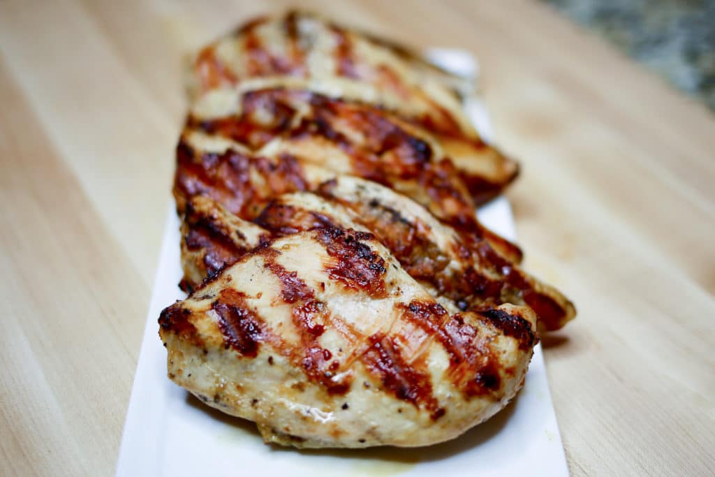 A white rectangular plate with 4 grilled chicken breasts