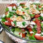 A clear bowl of salad with chicken, sliced tomatoes, feta cheese, and chopped parsley