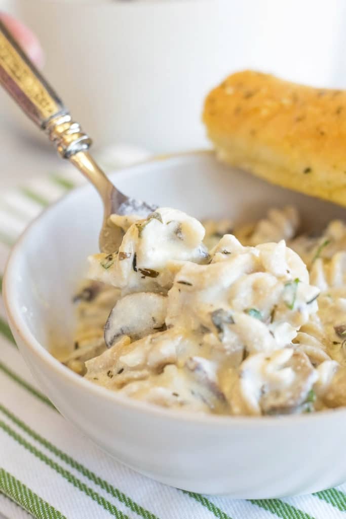 White bowl of mushroom and goat cheese pasta with bread stick and fork