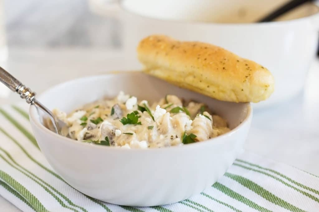 White bowl of mushroom and goat cheese pasta with breadstick