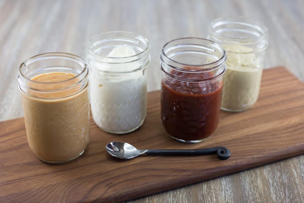 4 mason jars on a cutting board with different condiments