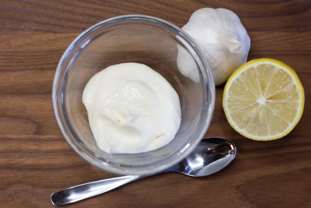 Bowl of mayonnaise, half of a lemon, bulb of garlic, and spoon