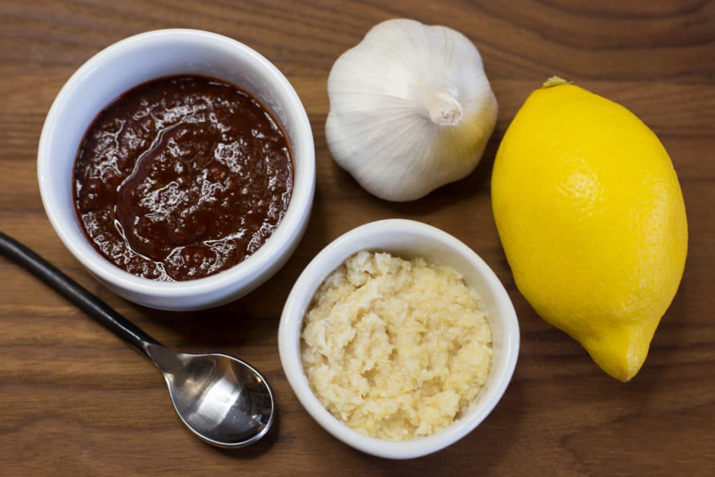 A lemon, a bulb of garlic, a small bowl of horseradish, and a small bowl of adobo sauce