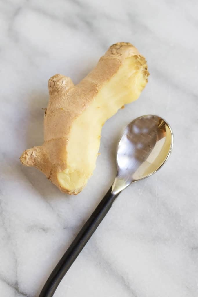 Overhead view of a partially peeled piece of ginger next to a spoon