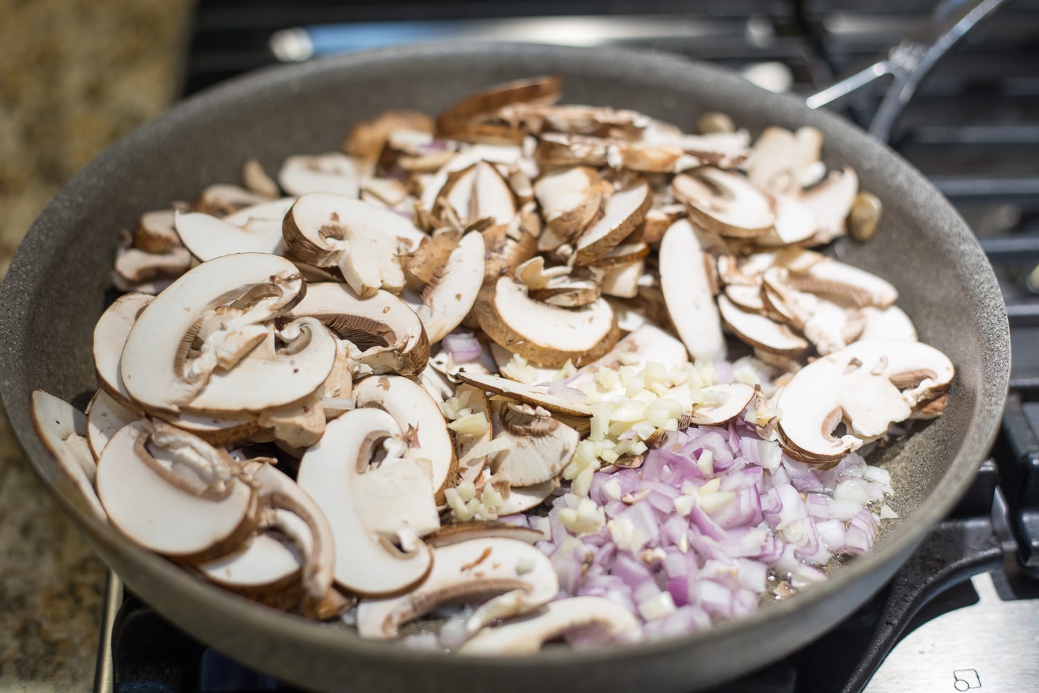 A gray skillet of diced shallots, sliced cremini mushrooms, and minced garlic 