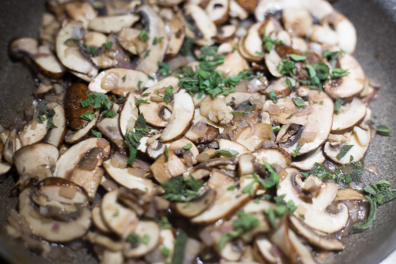 Up close view of a gray skillet of cooked cremini mushrooms and chopped sage