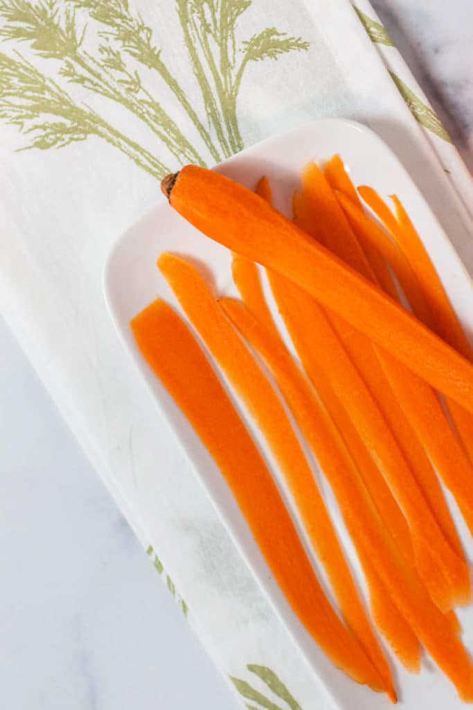 Overhead view of carrot strips on a white plate on top of a napkin