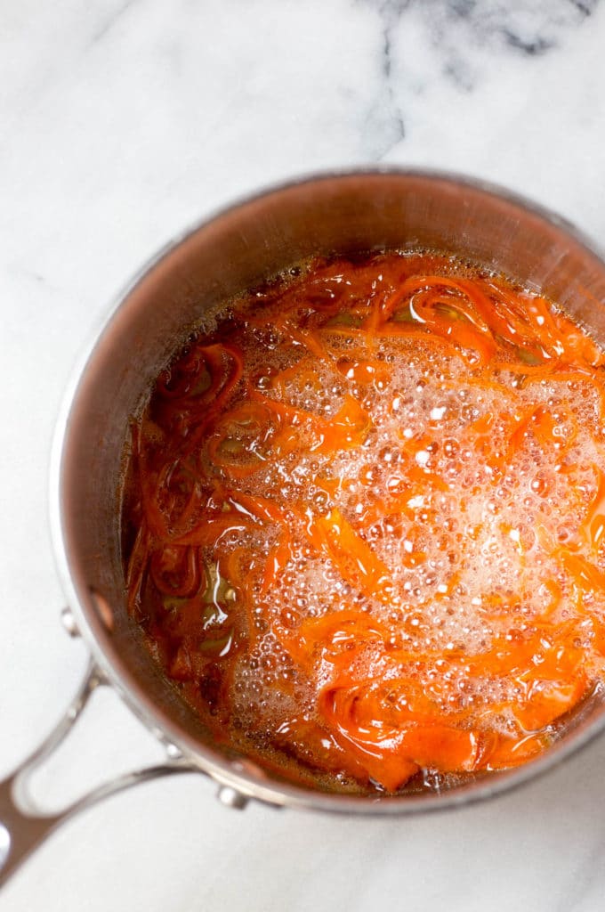 Overhead view of carrot strips boiling in simple syrup in a saucepan