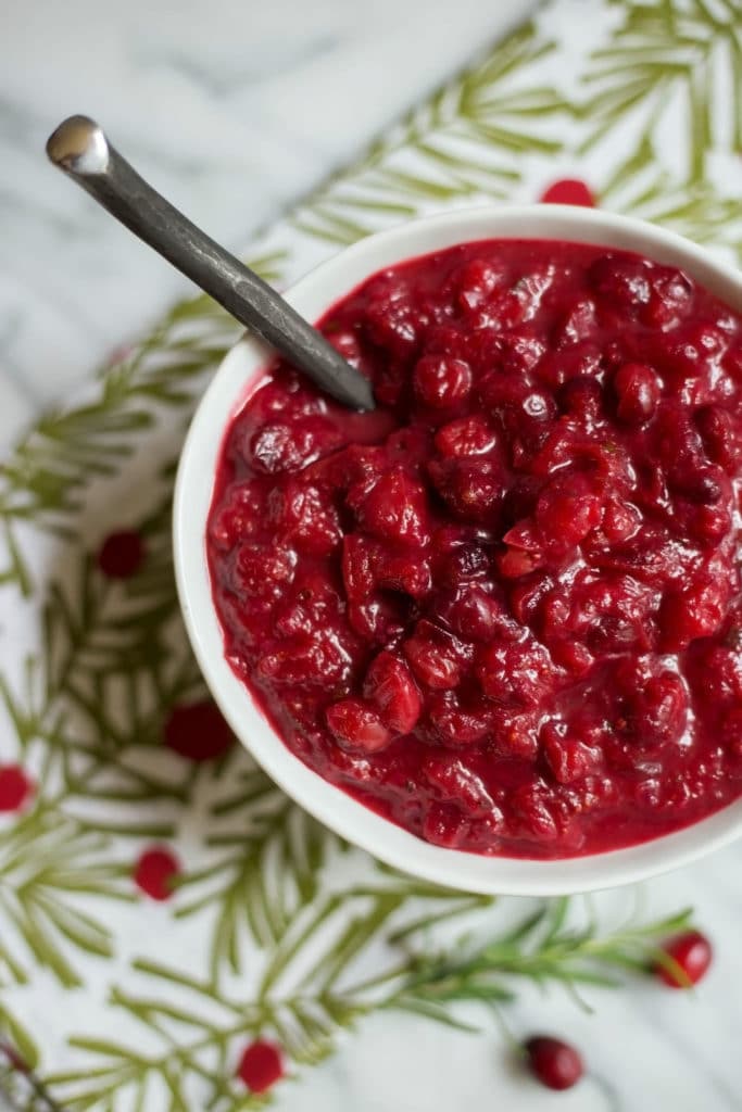 Overhead view of a white bowl of bright red cranberry sauce on a holiday napkin