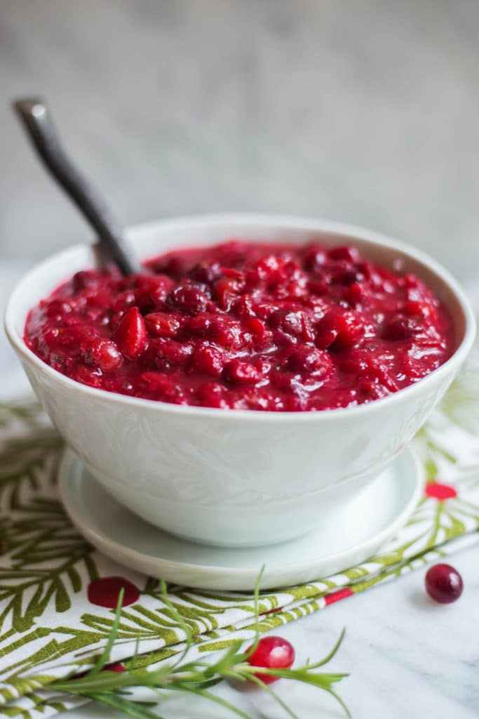 Side view of a white bowl of bright red cranberry sauce on a holiday napkin