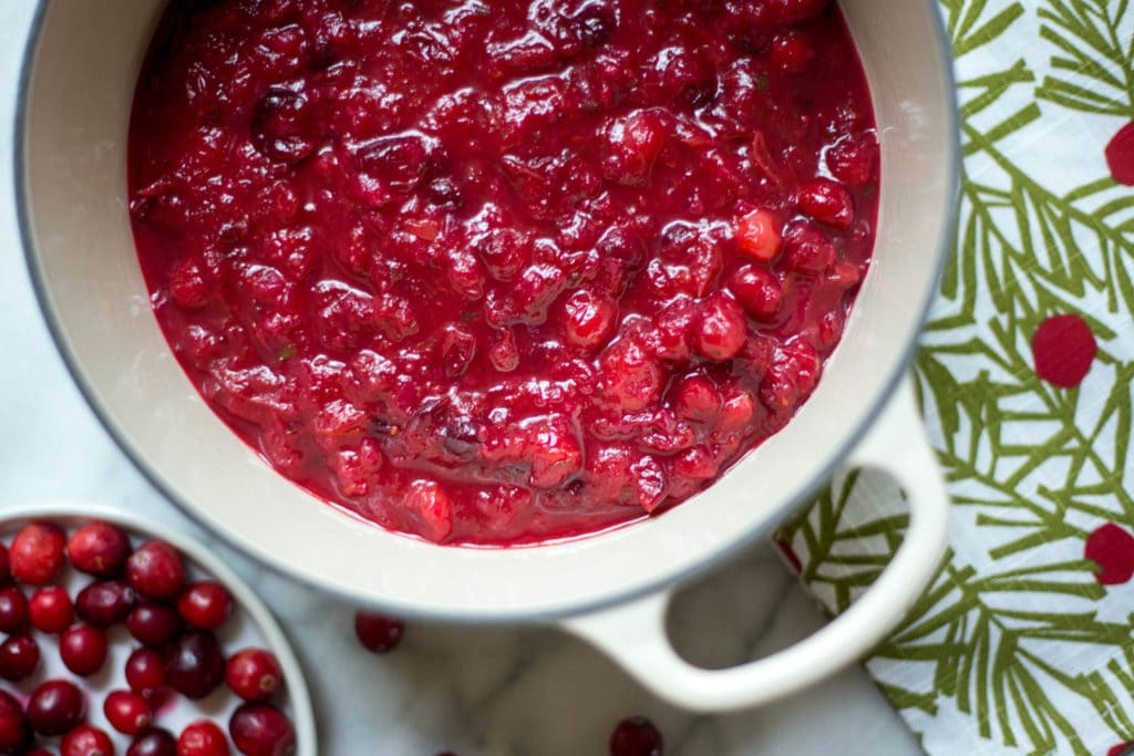 Overhead view of a white dutch oven filled with bright red cranberry sauce on a holdiday napkin
