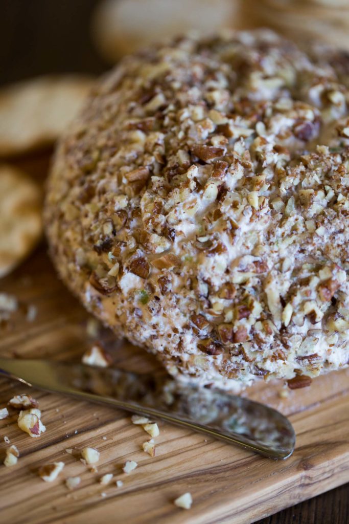 A cheese ball coated in pecan pieces on a wood cutting board next to a knife