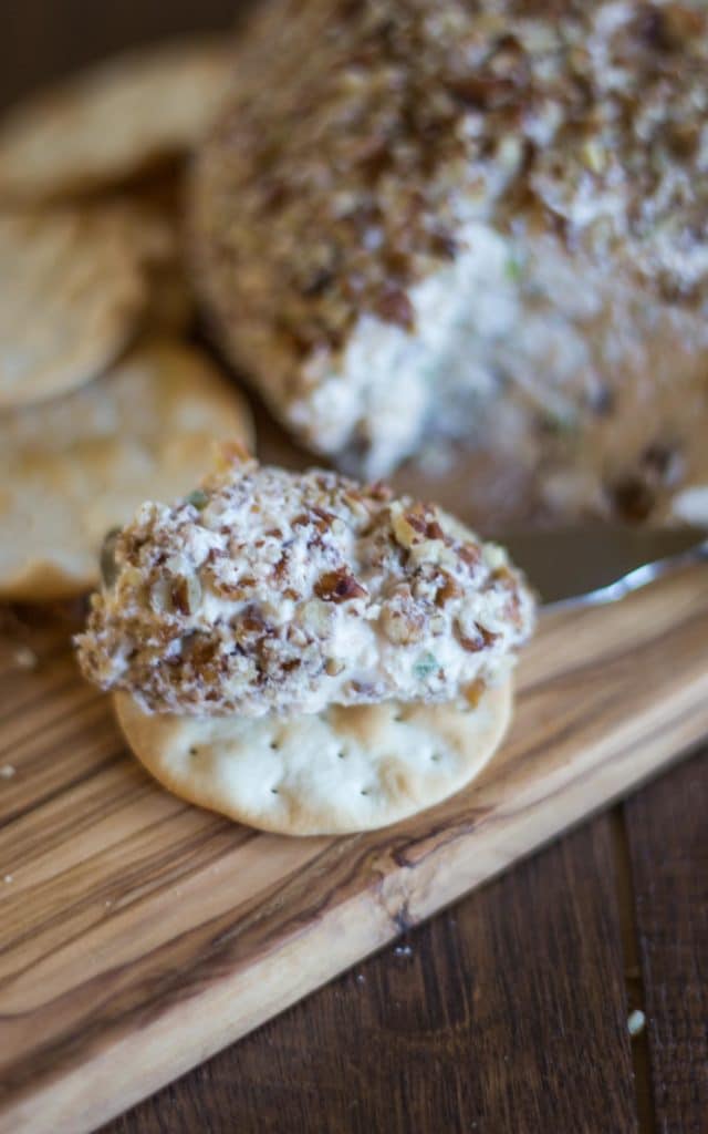 A cracker on a wood cutting board with cheese ball spread on it