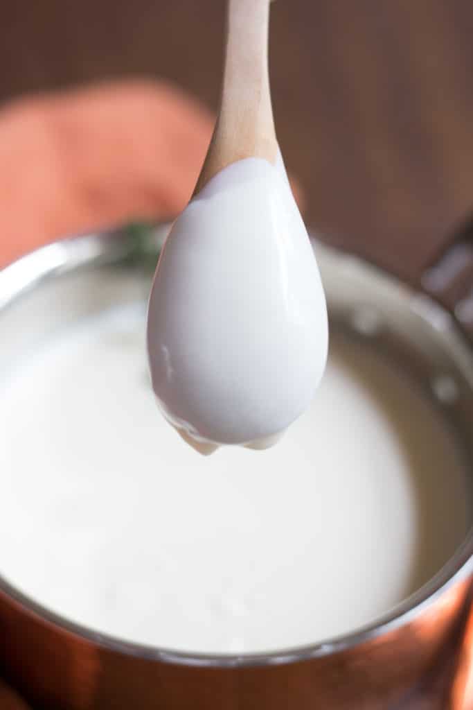 The back of a wooden spoon coated with bechamel sauce over a copper saucepan