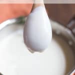 The back of a wooden spoon coated with bechamel sauce over a saucepan