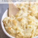 A white baking dish of baked cauliflower with a wooden spoon