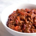 A white bowl of beef chili with chunks of tomato and beans