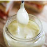 A spoon scooping mayonnaise from a clear jar