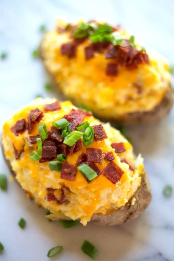 Two twice baked potatoes topped with melted cheddar cheese, bacon crumbles, and scallions