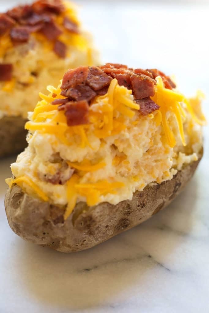 A potato boat filled with a mixture of mashed potatoes topped with cheddar cheese and cooked bacon