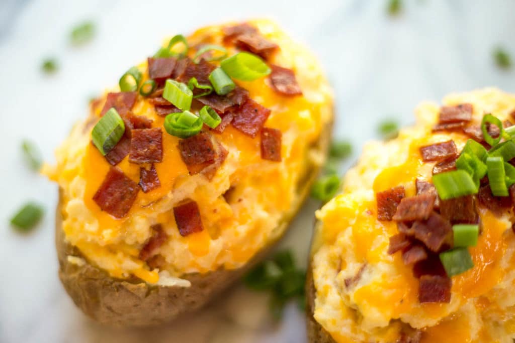 A twice baked potato topped with cheddar cheese, bacon crumbles, and scallions