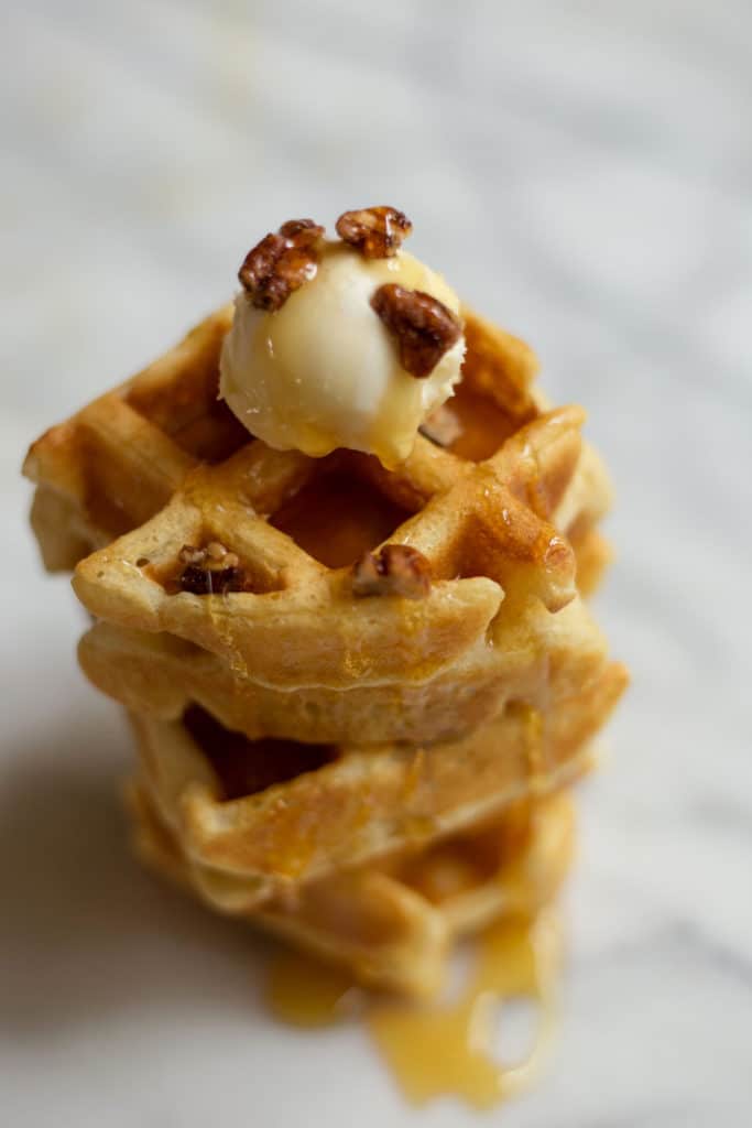 Stack of belgian waffles topped with mascarpone, nuts, and syrup